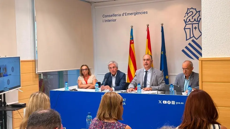 Persones davant un acte institucional, amb missatges sobre protecció davant emergències relacionades amb la DANA.